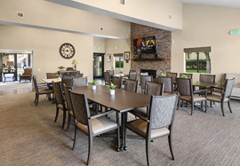 A large room with a dining table surrounded by chairs. The table is set for a meal with wine glasses, cups, and a vase. A television is mounted on the wall above the fireplace. AI generated content