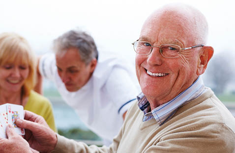 An older man is smiling while holding a deck of cards. AI generated content